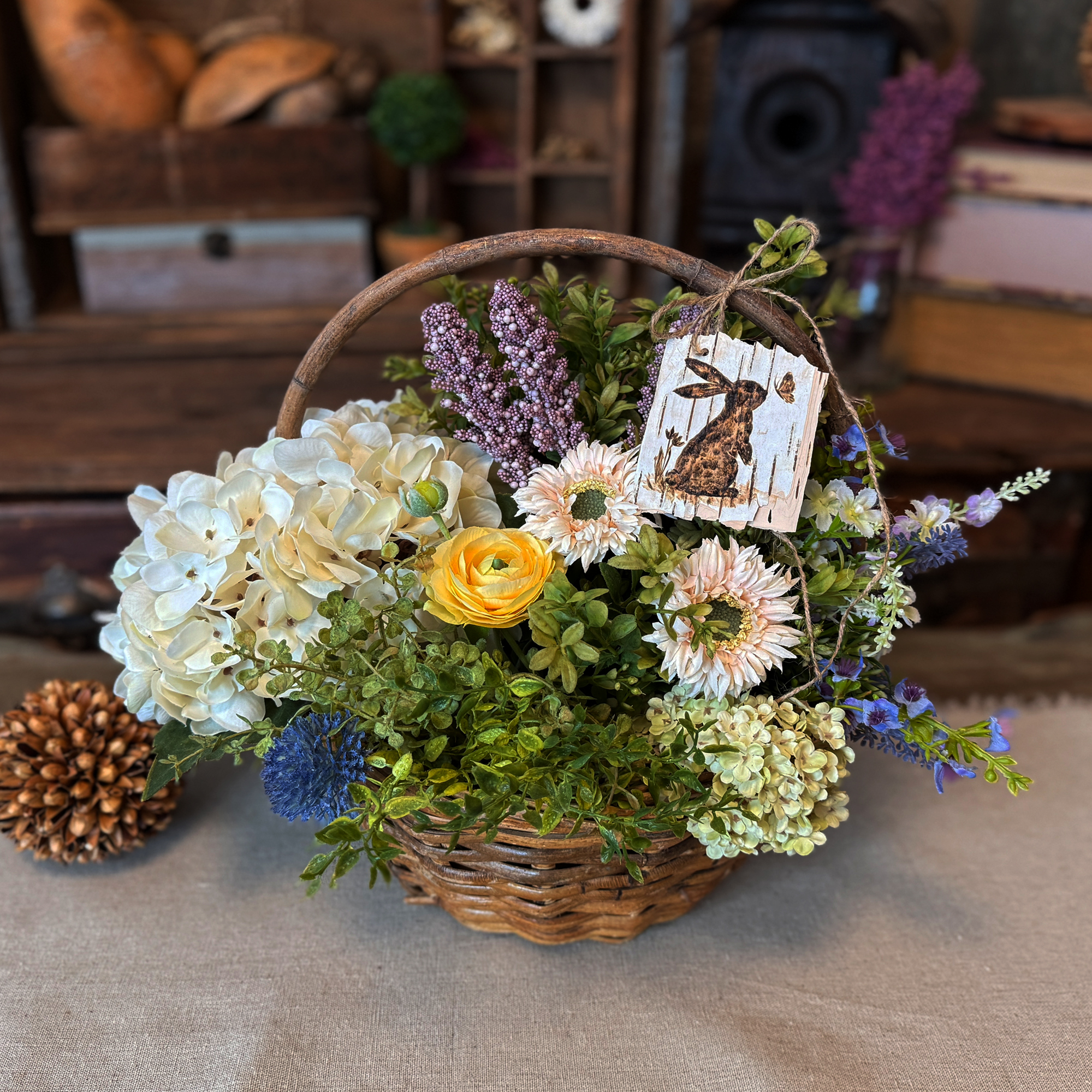 A spring gift basket full of faux flowers with a birch bark Easter bunny gift tag tied to the top.